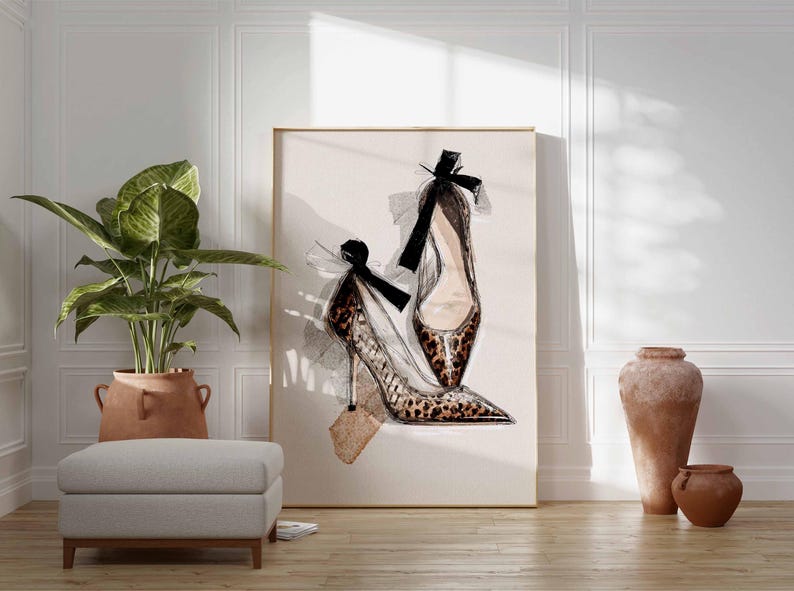 Op de afbeelding: Een kunstafdruk met een paar hoge hakken. E&eacute;n schoen heeft een luipaardprint en beide zijn versierd met zwarte strikken. Het kunstwerk is goudkleurig ingelijst en geplaatst tegen een neutrale achtergrond.