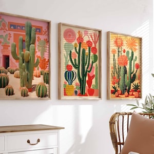 May include: Three framed illustrations of cacti in a desert landscape. The illustrations are in a retro style with bright colors and bold lines. The cacti are green, pink, and orange. The background is a light pink, yellow, and orange.