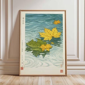 May include: A framed print featuring a serene water scene with yellow and green maple leaves floating on the surface. The water has a blue and white swirling pattern. Japanese text is visible on the left side of the print.