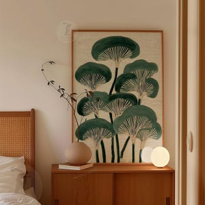 May include: A framed botanical print featuring stylized green mushroom illustrations on a beige background. The artwork is displayed above a wooden cabinet with a round beige vase, a book, and a small, round lamp.