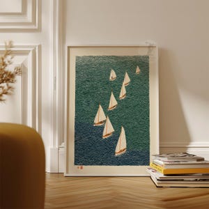 May include: A framed art print featuring a nautical scene with several sailboats on a textured teal and navy blue ocean. The sailboats have white sails and brown hulls. The print is displayed on a wooden floor.