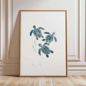 Peut inclure: Impression encadrée représentant trois tortues de mer turquoise sur fond blanc. Les tortues présentent des motifs de carapace détaillés. L'œuvre est encadrée dans un cadre en bois, pour une décoration côtière ou nautique.
