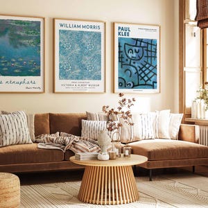 May include: A living room with a brown sofa, cushions, and a patterned rug. Three framed art prints are displayed above the sofa, including a Monet painting, a William Morris design, and a Paul Klee artwork. A wooden coffee table and a woven ottoman are also present.