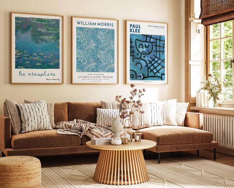 May include: A living room with a brown sofa, cushions, and a patterned rug. Three framed art prints are displayed above the sofa, including a Monet painting, a William Morris design, and a Paul Klee artwork. A wooden coffee table and a woven ottoman are also present.
