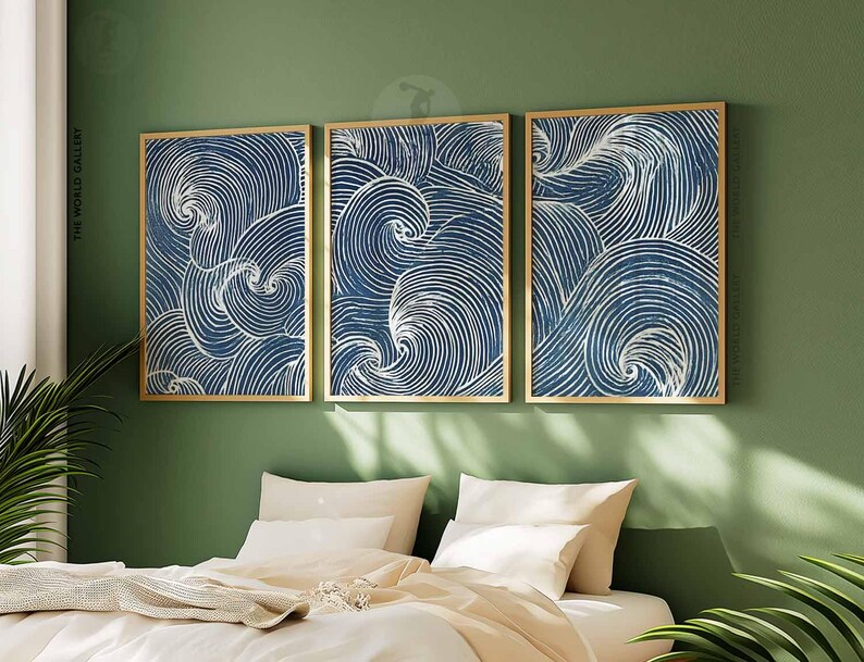 May include: Three framed wall art pieces with a blue and white wave pattern. The artwork is displayed on a green wall above a bed with white bedding. The frames are a light gold color.