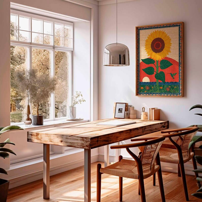 Op de afbeelding: Een rustiek houten bureau met metalen poten en twee geweven stoelen in een lichte kamer. Een ingelijst zonnebloemkunstwerk hangt aan de muur. Een groot raam biedt uitzicht op bomen en natuurlijk licht.