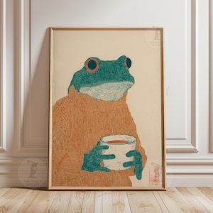 Può includere: Stampa artistica incorniciata con un'illustrazione di una rana con un maglione arancione che tiene in mano una tazza bianca. La rana è turchese con occhi arancioni e mani turchesi. La stampa ha un'estetica vintage.