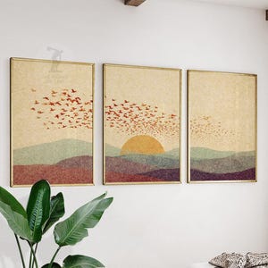 Puede incluir: Un conjunto de tres impresiones artísticas enmarcadas. Cada impresión presenta un paisaje con una puesta de sol, montañas y pájaros en vuelo. La paleta de colores incluye tonos cálidos de naranja, rojo y marrón, con una textura de papel vintage.