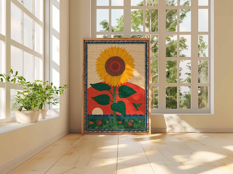 Op de afbeelding: Een ingelijst kunstwerk met een grote gele zonnebloem met een bruin centrum, groene bladeren en een rode zonsondergang achtergrond. Een kolibrie is onderaan afgebeeld. Het kunstwerk wordt tentoongesteld in een kamer met een raam en planten.