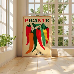 May include: A framed art print featuring a colorful illustration of chili peppers. The word "PICANTE" is at the top in red and green letters, with the word "chillies" at the bottom. The peppers are red, orange, green, and yellow.