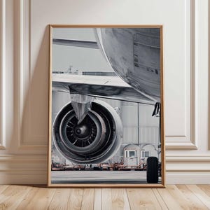 Könnte beinhalten: Gerahmter Druck mit einer detaillierten Ansicht eines Flugzeugtriebwerks und Flügels. Das Bild ist in Graustufen gehalten und hebt die metallischen Texturen und mechanischen Komponenten hervor. Der Fokus liegt auf dem komplizierten Design des Triebwerks und der Struktur des Flugzeugs.