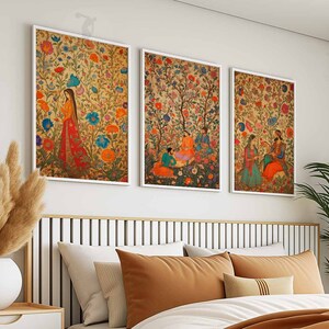 May include: Three framed prints with colorful floral patterns and figures in traditional Indian clothing. The prints are hung on a white wall above a bed with brown bedding.