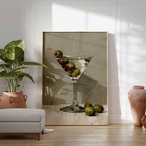 May include: A framed artwork depicts a martini glass filled with olives. The painting has a neutral color palette with a light background. A potted plant, a footstool, and terracotta vases are in the foreground.
