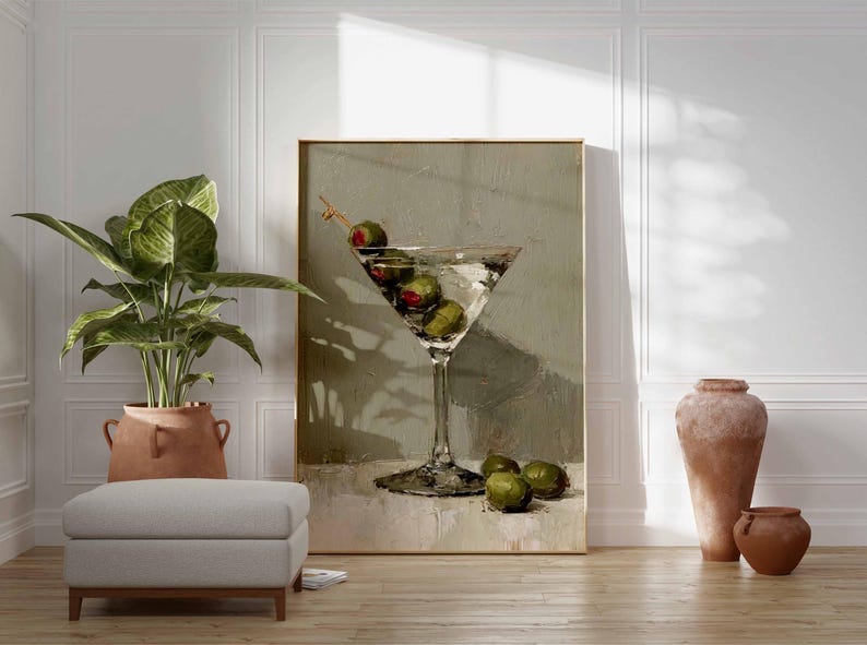 May include: A framed artwork depicts a martini glass filled with olives. The painting has a neutral color palette with a light background. A potted plant, a footstool, and terracotta vases are in the foreground.