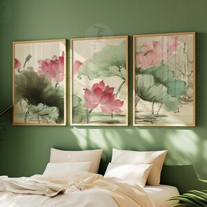 May include: Three framed art prints featuring watercolor paintings of pink lotus flowers and green leaves. The artwork is set against a neutral background, with gold frames. The prints are displayed on a green wall above a bed with white bedding.