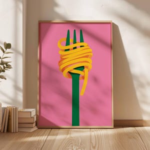 Op de afbeelding: Een ingelijste kunstprint met een groene vork met gele spaghetti op een roze achtergrond. Het kunstwerk heeft een minimalistische stijl, ideaal voor een keuken of eetkamer. De lijst is lichtbruin.