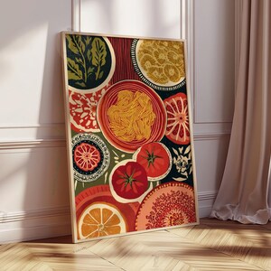 May include: A framed art print featuring a colorful still life of food. The artwork includes images of pasta, tomatoes, oranges, and decorative plates in shades of red, orange, green, and yellow. The print is leaning against a white wall and a wooden floor.