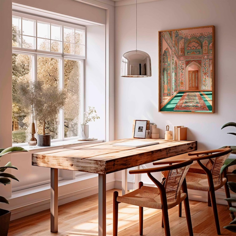 May include: A well-lit home office with a large wooden desk and two woven chairs. A framed artwork depicting an ornate interior scene hangs on the wall. A large window offers a view of the outdoors. A modern silver pendant light hangs above the desk.