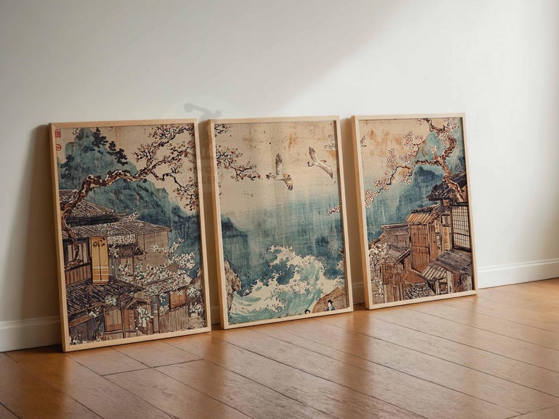 May include: Three framed prints of Japanese art depicting a traditional village with cherry blossoms and birds flying over a body of water. The prints are in a light wood frame and have a white background.
