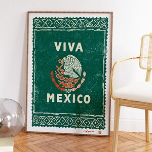 May include: A framed print featuring the Mexican coat of arms, with the words "VIVA MEXICO" in white on a green background. The print has a distressed, vintage look and is framed in a wooden frame.