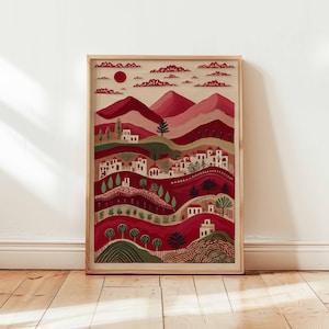 May include: A framed art print showing a stylized landscape with hills, houses, and trees. The colour scheme is mainly red, with a red sun and clouds in the sky. The artwork is presented in a natural wood frame.
