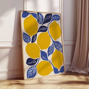 May include: A framed art print featuring a vibrant illustration of lemons and leaves. The lemons are yellow, and the leaves are blue, set against a cream background. The artwork is displayed in a light-colored wooden frame, leaning against a white wall and wooden floor.