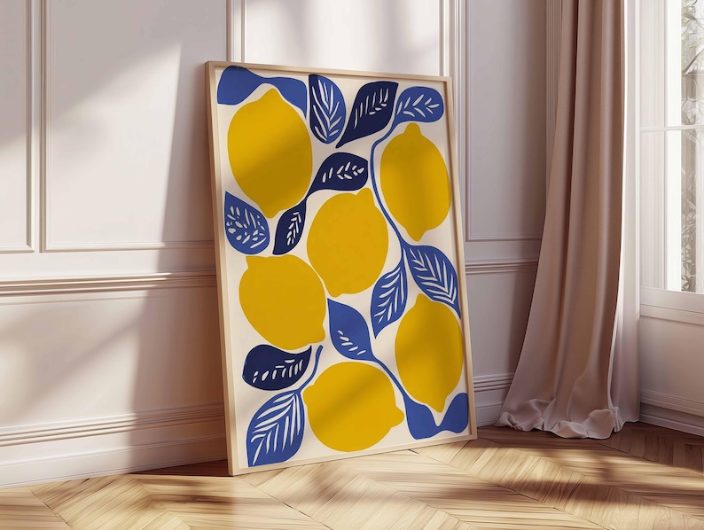 May include: A framed art print featuring a vibrant illustration of lemons and leaves. The lemons are yellow, and the leaves are blue, set against a cream background. The artwork is displayed in a light-colored wooden frame, leaning against a white wall and wooden floor.
