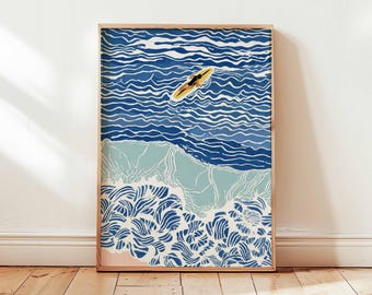 May include: A framed art print depicting a person on a yellow surfboard in blue ocean waves. The artwork features a stylized illustration of the sea with white, light blue, and dark blue tones. The print is in a wooden frame.
