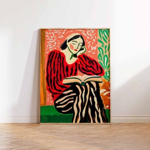 May include: A framed painting of a woman in a red and black striped shirt and pants sitting and reading a book. The background is a pink and green abstract design.