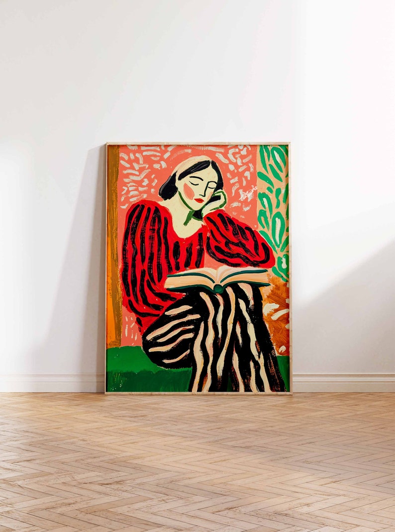 May include: A framed painting of a woman in a red and black striped shirt and pants sitting and reading a book. The background is a pink and green abstract design.