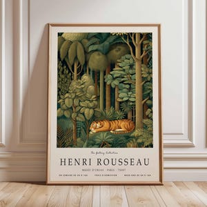 Puede incluir: Una impresi&oacute;n art&iacute;stica enmarcada que representa una escena de la jungla con un tigre. La obra de arte, de Henri Rousseau, presenta una exuberante vegetaci&oacute;n verde, &aacute;rboles altos y un tigre a rayas naranjas y negras. El texto en la parte inferior dice "HENRI ROUSSEAU".