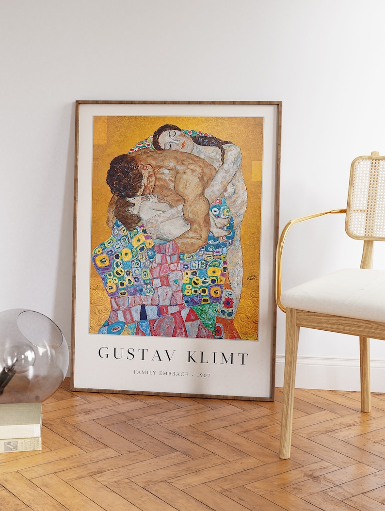 May include: A framed poster of Gustav Klimt's painting "Family Embrace" from 1907. The painting depicts a family in a warm embrace, with a mosaic-like pattern on the woman's dress. The poster has a gold frame and a white background with the artist's name and the title of the painting.