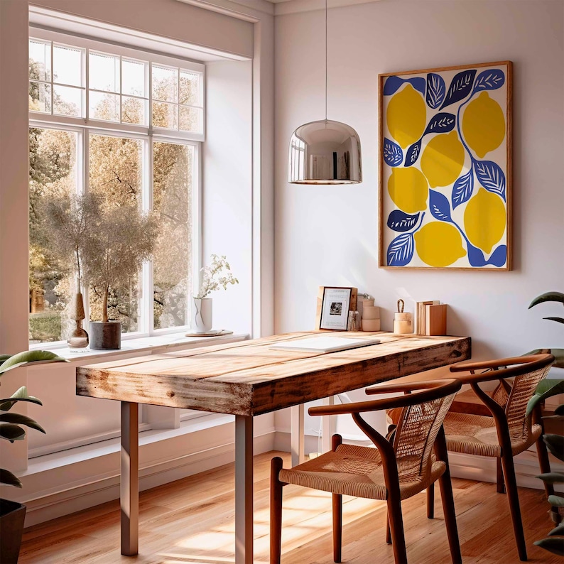 May include: A bright, airy room with a wooden desk and two woven chairs. A framed lemon print hangs on the wall. A large window offers a view of trees. A silver pendant light hangs above the desk.