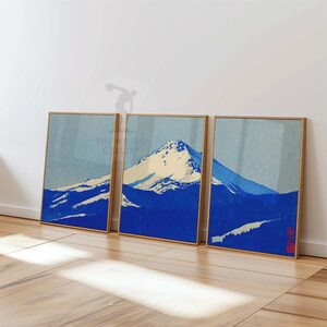 K&ouml;nnte beinhalten: Drei gerahmte Drucke mit einer Berglandschaft in Blau- und Cremet&ouml;nen, im Stil japanischer Holzschnitte. Die Rahmen sind helles Holz. Die Drucke lehnen an einer wei&szlig;en Wand.