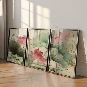 May include: Three framed art prints featuring watercolor paintings of pink lotus flowers and green leaves. The artwork has a traditional Asian style, with soft colors and delicate brushstrokes. The frames are black.