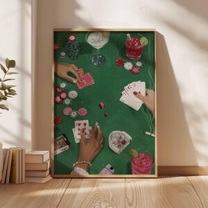May include: A framed art print depicting a poker game scene. The artwork features a green felt table with playing cards, poker chips, dice, and cocktails. Hands with jewelry are visible, holding cards and chips. The overall color palette is green, red, and white.