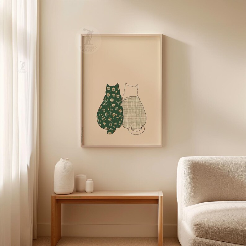 Puede incluir: Un cuadro enmarcado con dos gatos estilizados. Uno es verde con un estampado floral, el otro beige con un patr&oacute;n texturizado. La obra se presenta sobre un fondo beige, dentro de un marco de madera. El cuadro est&aacute; colgado en una pared beige claro.