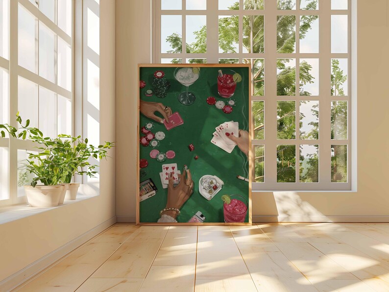 May include: A framed art print depicts a poker game scene on a green felt table. Hands are holding playing cards, poker chips, and cocktails. The artwork is set against a bright window and wooden floor.