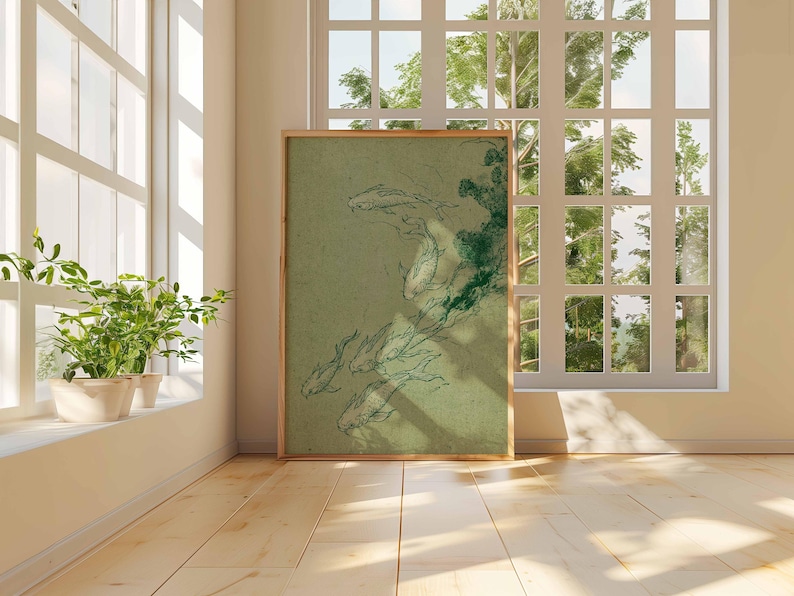May include: A framed art print featuring a green and white illustration of koi fish. The artwork is displayed on a wooden floor, leaning against a wall near a window. The room has a neutral color palette with natural light.