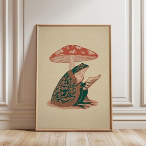 Peut inclure: Impression d'art encadrée. Une grenouille verte portant des lunettes et une robe à motifs lit sous un champignon rouge. L'illustration a une esthétique vintage avec un fond beige et un cadre en bois. Design fantaisiste.