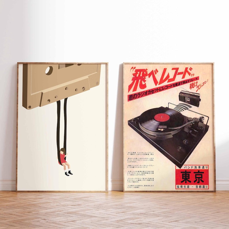 Op de afbeelding: Twee ingelijste posters op een houten vloer. De poster aan de linkerkant toont een cartoonillustratie van een cassetteband met een persoon die eraan hangt. De poster aan de rechterkant toont een vintage advertentie voor een platenspeler met de tekst "飛べレコード" in rood.