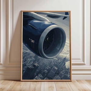 Könnte beinhalten: Gerahmter Kunstdruck mit einem detaillierten Blick auf ein Flugzeugtriebwerk vor dem Hintergrund einer Stadtlandschaft und Wolken. Das Triebwerk ist hauptsächlich dunkelblau und silber, die Stadt in Grautönen dargestellt.