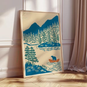 May include: A framed art print featuring a teal and beige illustration of a forest scene. The artwork depicts mountains, trees, a lake, and a bear in a small orange boat. The print is displayed against a white wall and wooden floor.