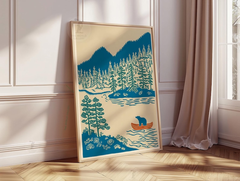 May include: A framed art print featuring a teal and beige illustration of a forest scene. The artwork depicts mountains, trees, a lake, and a bear in a small orange boat. The print is displayed against a white wall and wooden floor.