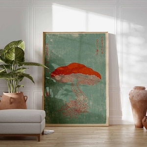 May include: A framed art print featuring a large red mushroom against a teal background. The artwork has Japanese text and is displayed in a room with a potted plant, a gray ottoman, and decorative pottery.