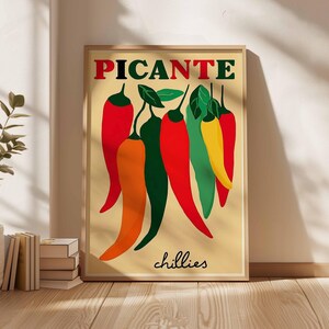 May include: A framed art print featuring a stylized illustration of chili peppers. The word "PICANTE" is at the top in red letters, with the word "chillies" at the bottom. The peppers are in shades of red, orange, green, and yellow.