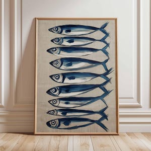 Puede incluir: Una impresión artística enmarcada que presenta una representación estilizada de ocho peces azules dispuestos verticalmente. Los peces están pintados con un efecto de pincelada sobre un fondo neutro, creando un tema náutico o costero. La obra de arte está dentro de un marco de madera.