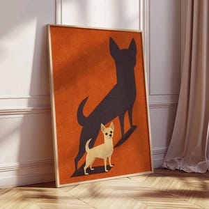 May include: Framed art print featuring a light tan chihuahua with a black shadow on an orange background. The artwork is in a wooden frame and leans against a white wall and wooden floor. The print has a minimalist, modern design.