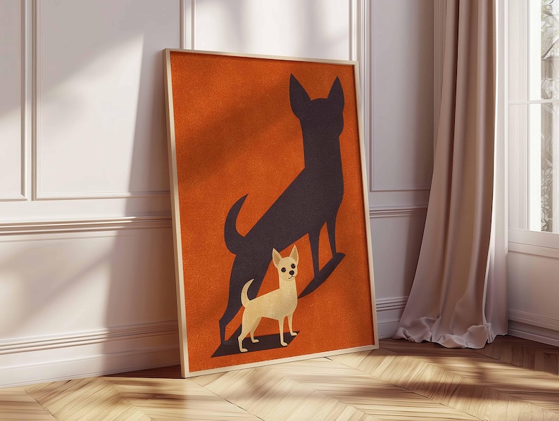 May include: Framed art print featuring a light tan chihuahua with a black shadow on an orange background. The artwork is in a wooden frame and leans against a white wall and wooden floor. The print has a minimalist, modern design.