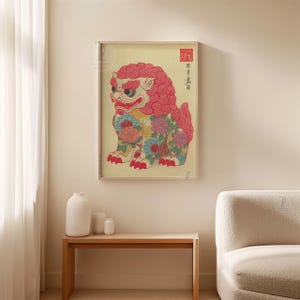 May include: Framed print of a colorful, stylized lion-dog. The artwork features a red mane and floral patterns in blue, yellow, and pink. The print includes Japanese text and a red seal, set against a cream background.